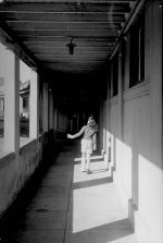 Long shot taken from behind of a young patient walking down an outside corridor. In the Walkways, Circa 1955