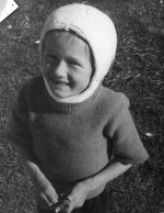 Close up shot of a young child smiling for the camera. The child has a plaster cast on their head that extends around their chin. Smiling Child with Cast, Circa 1955