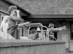 Long shot of a group of nurses and patients standing outside on a balcony. One person is looking through a pair of binoculars and the others are pointing to the sky. Watching from the Balcony, Circa 1955