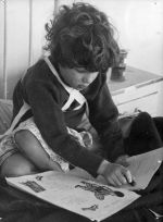 A close shot of a child sitting on a bed drawing in a book. Reading in Bed, Circa 1955