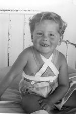 A medium shot of a young child sitting on a bed smiling at the camera. Portrait of a Child, Circa 1955