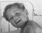 A close up shot of a young child in a bed, smiling at the camera. Portrait of a Child, Circa 1955