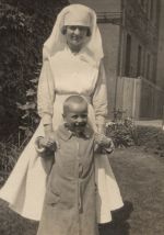 Long shot of a staff member holding the hands of a patient who is standing in front of her, the staff member and patient are outside, the exterior of the building can be seen on the right side of the photograph. Nurse and Patient, 1922