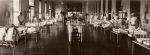 Long shot of hospital room. Beds are positioned along walls and staff members are standing in close proximity to beds. There are patients in beds. There is a central table which contains multiple vases with flowers. Ormond Ward, Circa 1918