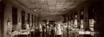 Long shot of interior of hospital room. Beds are positioned along walls, staff are present throughout the room while there are patients standing, sitting and in beds. Ormond Ward, Circa 1918