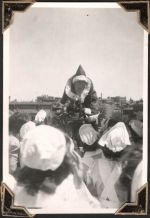 Long shot of a man in Father Christmas costume standing on top of a vehicle outside. Several staff members stand between the camera and the man. We can see the back of their bonnets. Christmas Time, Circa 1945