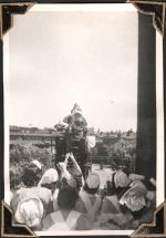 Long shot of a man in Father Christmas costume standing on top of a vehicle outside. Several staff members stand between the camera facing the man. We can see the back of their bonnets. Christmas Time, Circa 1945