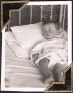 Medium shot of an infant patient lying in a hospital crib. They are framed to the right of the photograph, lying on their back, head turned to the left. Small Child in Bed, Circa 1945