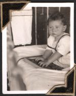 Medium shot of an infant patient sitting in their crib playing with a puzzle toy. There is a towel hung over the side of the crib. Small Child in Bed, Circa 1945