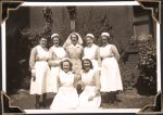 Long shot of seven female staff in uniform standing outside. A brick wall and plants can be seen behind them. Staff Portrait, Circa 1945
