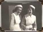 Medium shot of two staff members in uniform inside a room with a brick wall and curtain. Two Nurses, Circa 1945