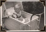 Medium shot of an infant in a pram with blankets and a soft toy. Some greenery can be seen in the background. Infant in Pram, Circa 1945