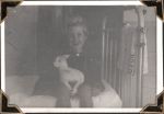 Medium shot of a young child sitting on the side of a bed, with a toy lamb in their lap. The child is smiling. Child with Toy, Circa 1945
