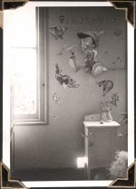 Medium shot of a patient room with heavy focus on the Pinocchio wall art. Some of a window sill can be seen and there is a small cabinet to the right which features a cat toy on top. Pinocchio Wall Art, Circa 1945
