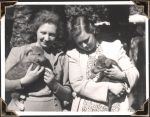 Medium shot of two women standing, each holding a puppy. Puppies, Circa 1945