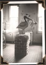 Medium shot of room. End of hospital bed visible on left hand side. Two windows at end of room. Pinocchio wall art visible between the windows. In foreground on floor is a fake chimney with a toy stork holding a sling with a doll inside it's beak. Ward 16 Stork, Circa 1945