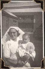 Medium shot of Nurse Buxton standing outside buildings, holding infant in front of her. Nurse and Child, Circa 1945