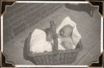 Medium shot of infant tucked into large basket. A brick wall is visible behind basket. Baby in Basket, Circa 1945