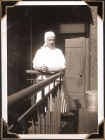 Medium shot of a staff member standing on a landing dressed in head covering and gown. Nurse Near the Dispensary, Circa 1945