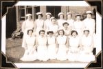 Medium shot of fifteen staff members in a group outside building; six kneeling in front row, two crouching in second row and seven standing in back row. Staff Portrait, Circa 1945