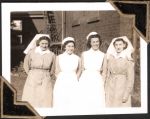 Medium shot of four staff members standing side by side outside building. Nurses Outside, Circa 1945