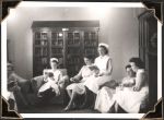 Medium shot of six seated staff members, reading books. A bookshelf with glass doors is in the background. Nurses Lounge, Circa 1945