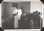 Medium shot of a staff member standing behind machinery holding equipment connected with a wire wearing a white medical gown. X-Ray, Circa 1945