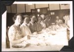 Medium shot of eleven medical staff in casual clothes sitting at the long table. The table is set for eating with dinnerware, cutlery and salt. The photo is taken at an angle that showcases one side of the table. Lunch Time, Circa 1945