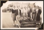 Long shot of seven women in casual dress standing around a trolley. The view of a street can be seen in the background. Flowers for Christmas Day, Circa 1945