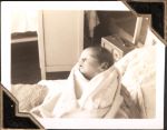 Close up of a new born baby being held by someone out of shot. A curtain and some furniture can be seen in the background. Newborn Baby, Circa 1946