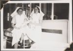 Medium shot of two staff members in uniform sitting down, each holding infant patients. There are windows into other infant rooms in the background. Women's Hospital, Circa 1946