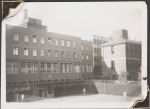 Long shot of three multiple story buildings and an area surrounding by wire fence and hedges. One building is mainly featured while two are in the background. There are some adults dressed in white in the foreground. Women's Hospital, Circa 1946