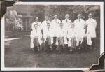 Long shot of eleven staff members wearing lab coats. Six stand in the back row and five sit in front. They are outside on grass, a building and trees are seen in the background. Women's Hospital, Circa 1946