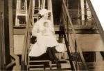 Long shot of a Nurse holding an infant seated on stairs outside posing for the camera. Nurse Holding a Baby, 1928