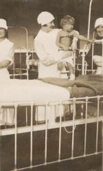 Long shot of three Nurses standing beside a cot, one Nurse is holding a young patient posing for the camera. Patients and Nurses, 1928