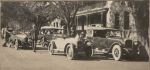 A long shot of a street with adults seated and beside cars. Automobiles, 1928