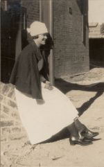 A long shot of a Nurse sitting outside on a brick wall. She has a cape around her shoulders. Portrait of a Nurse, 1928