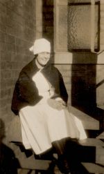 A long shot of a Nurse sitting outside on a table. She has a cape around her shoulders. Portrait of a Nurse, 1928