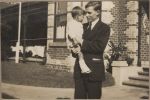 A medium shot of a man standing outside a building holding a child. Doctor and Child, 1928