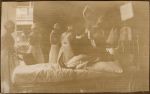 A long shot of a person dressed as Father Christmas standing beside a bed with a patient. There are four Nurses standing around watching. Christmas Celebrations, 1928