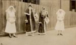 A long shot of two Nurses and two people dressed as Father Christmas standing outside in front of a paling fence. Father Christmas and Nurses, 1928