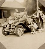 A long shot of two people dressed as Father Christmas. One is standing the other is sitting on a car that has been decorated with balloons and streamers. Christmas Celebrations, 1928