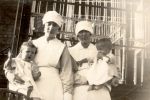 Medium shot of two Nurses holding a young patient and an infant outside posing for the camera Nurses Holding Babies, 1928
