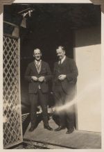A long shot of a two men standing outside at the entrance of a building. Two Males Standing Outside, 1928