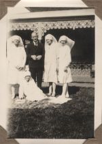 A long shot of three Nurses standing with a man and a fourth Nurse sitting on a rug on the grass. Staff on the Lawn, 1928