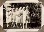 A long shot of seven Nurses standing in a row in a garden. Group Portrait, 1928