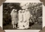 A long shot of seven Nurses in a garden. Five are standing and two are sitting in front on the grass. Staff on the Lawn, 1928