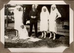 A long shot of three Nurses standing with a man in a garden. A Nurse is sitting on a rug at their feet. Staff on the Lawn, 1928