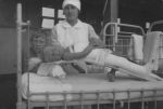 Long shot of a Nurse with two children. One child is in a cot with a lower body cast and is elevated via a stretcher. Nurse and Patients, Circa 1940