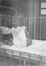 Long shot of an infant sitting in a cot. Dinner Time, Circa 1940